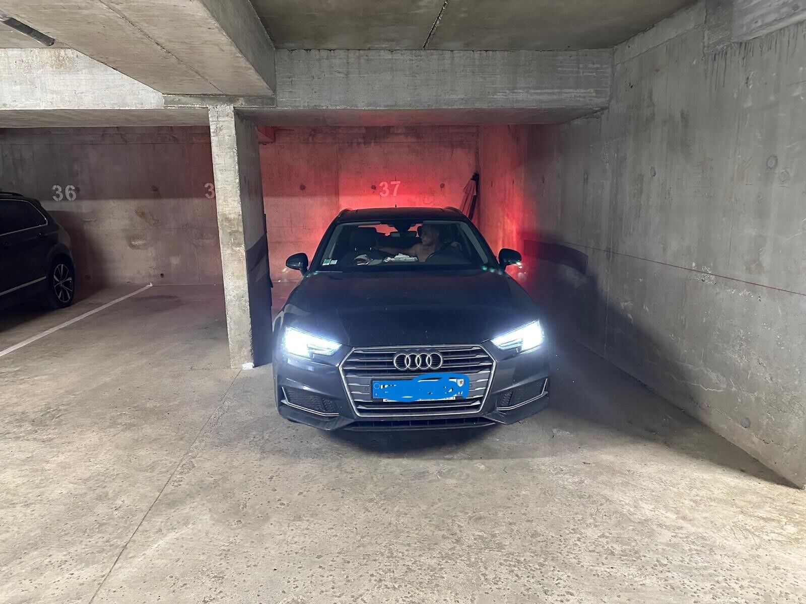 A black car parked in a concrete parking garage with visible numbers 36 and 37 on the walls.