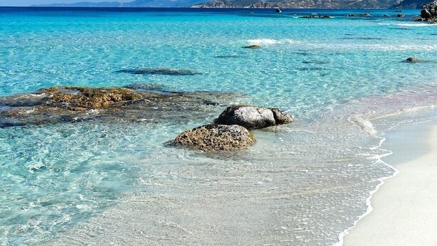 A beach with clear turquoise water, white sand, and rocky outcrops.