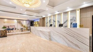 Un vestíbulo de hotel con un mostrador de recepción de mármol, una escalera y una zona de espera con televisión.