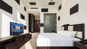 Habitación de hotel moderna con una cama grande, televisión, escritorio y un baño visible a través de una puerta de cristal.