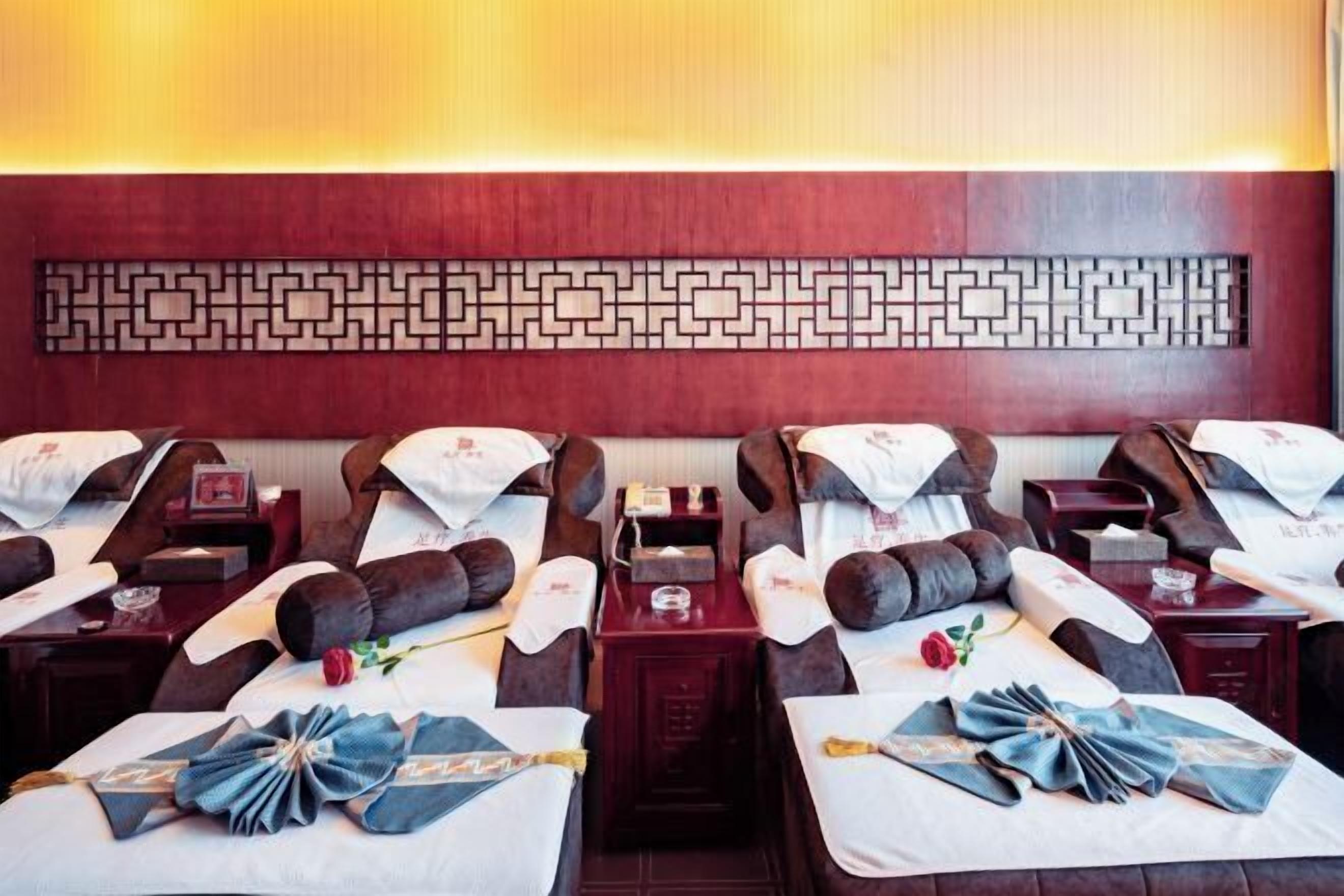 A hotel room with four beds arranged in a row, each with a pillow and a small table.