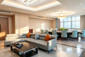 A modern hotel lobby with a sectional sofa, a coffee table, and a dining area with chairs and a table.