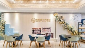 Vestíbulo de hotel con recepción, zona de estar con mesas y sillas, y pared decorativa con logotipo e imágenes.