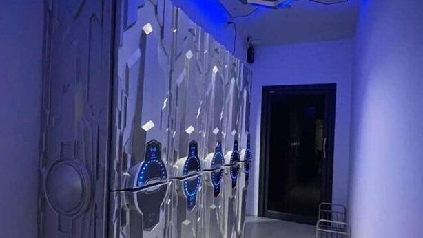 A modern room with a metallic wall and a door with illuminated blue lights. - PERA Space Capsule Hotel (Phuket)