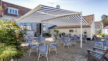 Una terrazza esterna con tende a righe blu e bianche, mobili in vimini bianco e piante in vaso.
