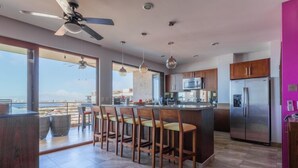 A modern kitchen with a central island, bar stools, stainless steel appliances, and large windows offering a view. - Residences by Pinnacle Unit 501 3BD Condo for rent in Old Town, Puerto vallarta (Puerto Vallarta)