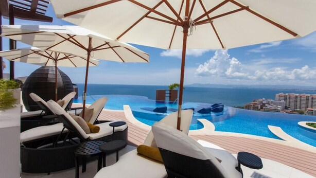 A rooftop lounge area with multiple sun loungers, umbrellas, and a view of a infinity pool overlooking the ocean. - Residences by Pinnacle Unit 501 3BD Condo for rent in Old Town, Puerto vallarta (Puerto Vallarta)