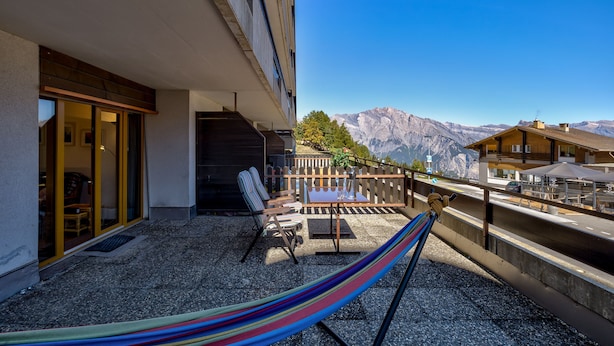 Ein Balkon mit Hängematte, Sitzgelegenheit im Freien und Blick auf die Berge.