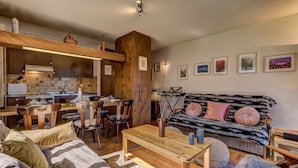 Ein gemütliches Wohnzimmer mit einem Holztisch, einer Couch mit gemusterten Kissen und einem Essbereich mit Holzsesseln und Tisch.