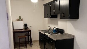 A compact kitchen with black cabinets, a gas stove, a coffee maker, and a ceiling fan. - Home away from home (San Felípe)