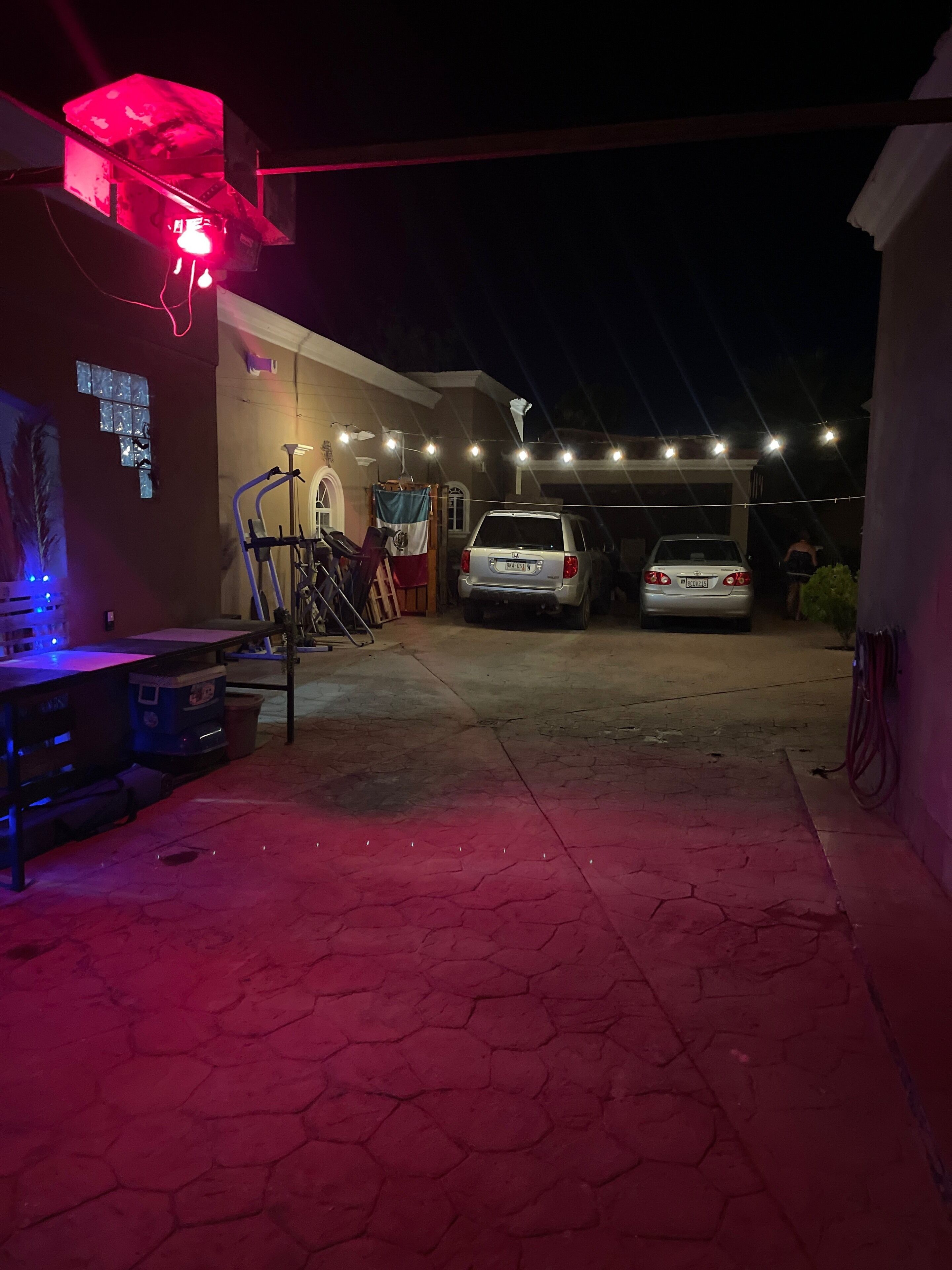 Een parkeerplaats 's nachts met twee auto's, een fiets en een gebouw met rode verlichting.