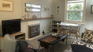 A living room with a TV, fireplace, dining table, and chairs. - Baxter's Vintage Chic BnB (Clare)