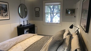 A bedroom with a bed, bedside table, lamp, window, and wall-mounted mirror. - Baxter's Vintage Chic BnB (Clare)