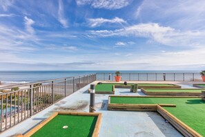 Terraço com grama sintética, vista para o mar e guarda-corpo de metal.