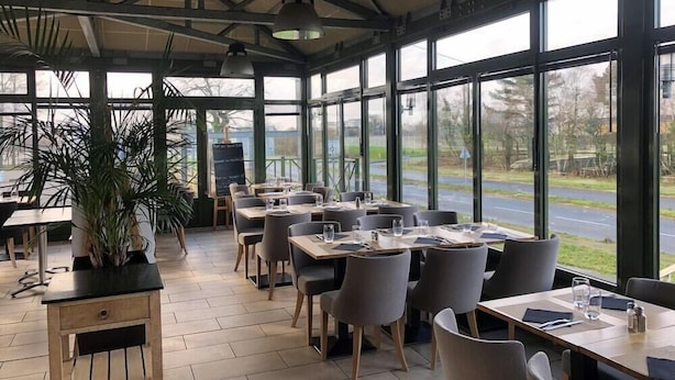Ein Restaurant mit großen Fenstern, gedeckten Tischen und einem Blumentopf.