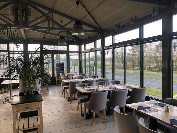 Ein Restaurant mit großen Fenstern, gedeckten Tischen und einem Blumentopf.