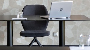 Ein moderner Arbeitsplatz mit einem Glastisch, einem schwarzen Stuhl und einem HP-Laptop.
