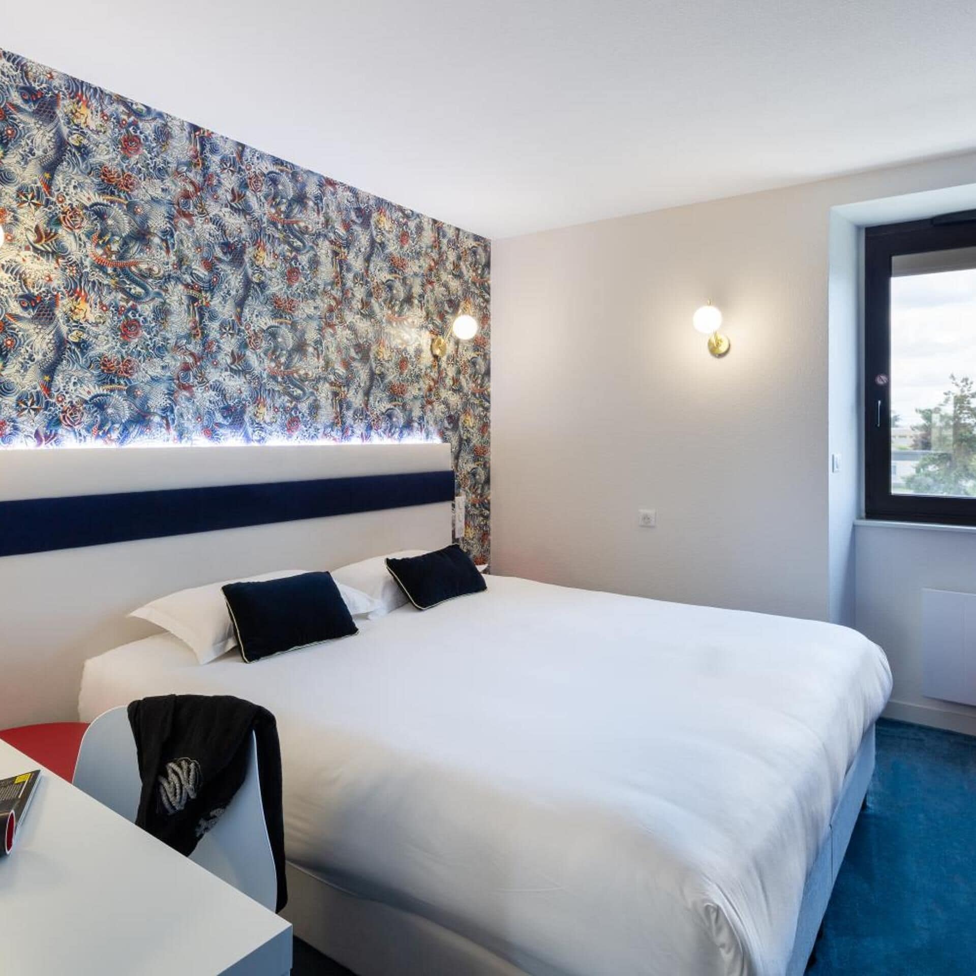 A hotel room with a large bed, two bedside lamps, a window, and a colorful abstract wall art.