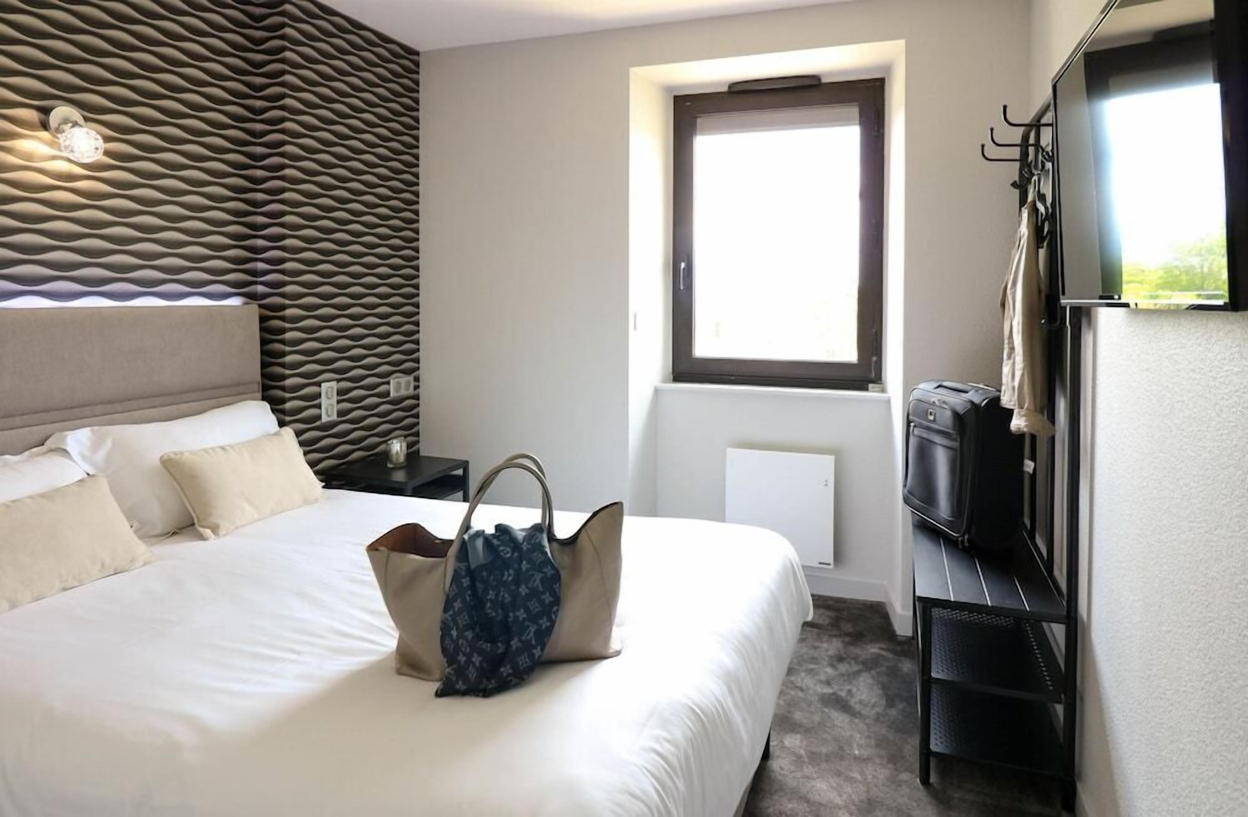 Quarto de hotel com cama, uma janela grande, televisão de tela plana e televisão fixada na parede.