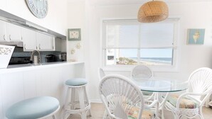 A kitchen with white cabinets, a stainless steel range hood, and a window overlooking the beach.