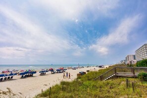 Een strand met parasols, een houten looppad en een gebouw op de achtergrond.