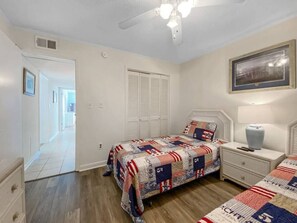 A bedroom with a bed, nightstand, and a ceiling fan. There is a door leading to another room.