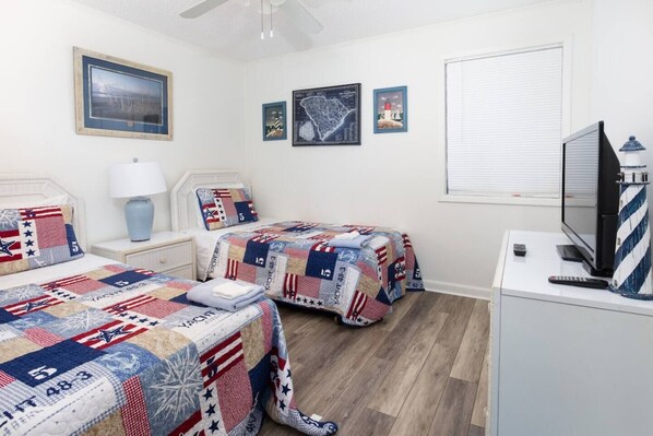 A bedroom with two beds, a television, and a window with blinds.