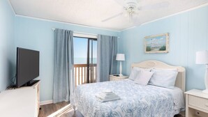A bedroom with a bed, a television, a nightstand, a lamp, a painting, and a view of the outdoors.