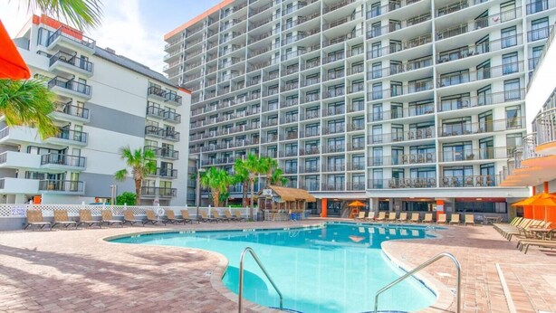 A hotel with a swimming pool, multiple balconies, and lounge chairs. - Hot Tubs & Indoor Pools - First-Floor Privacy (Myrtle Beach)