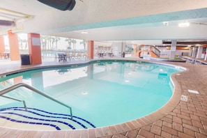 An indoor swimming pool with a tiled edge, a set of stairs leading into the pool, and a patio area with tables and chairs. - Hot Tubs & Indoor Pools - First-Floor Privacy (Myrtle Beach)