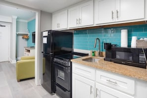 A modern kitchen with white cabinets, a black refrigerator, a stove, a sink, and a microwave.