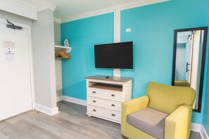 A room with a teal wall, a white dresser with drawers, a yellow armchair, and a flat-screen TV mounted on the wall. - Hot Tubs & Indoor Pools - First-Floor Privacy (Myrtle Beach)