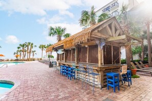 Un espace bar aménagé au bord de la piscine, avec des chaises et des tables, une piscine et des palmiers.