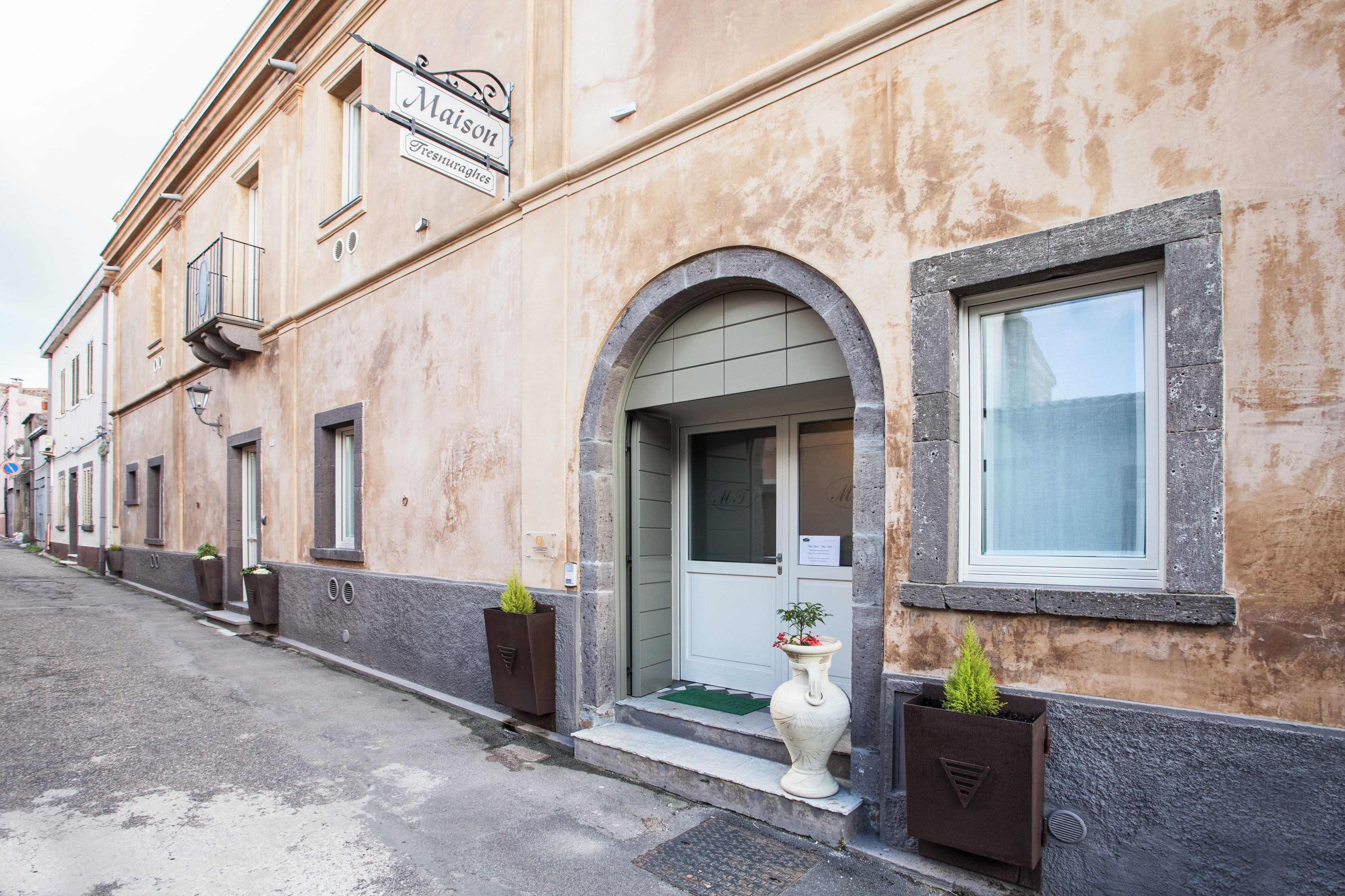 Un edificio con un cartello 'Maison Freshurglies' e un ingresso con tappetino verde. Ci sono fioriere con piante sul marciapiede.