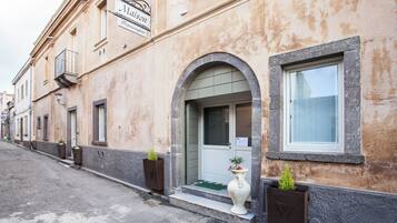 Un edificio con un cartello 'Maison Freshurglies' e un ingresso con tappetino verde. Ci sono fioriere con piante sul marciapiede.