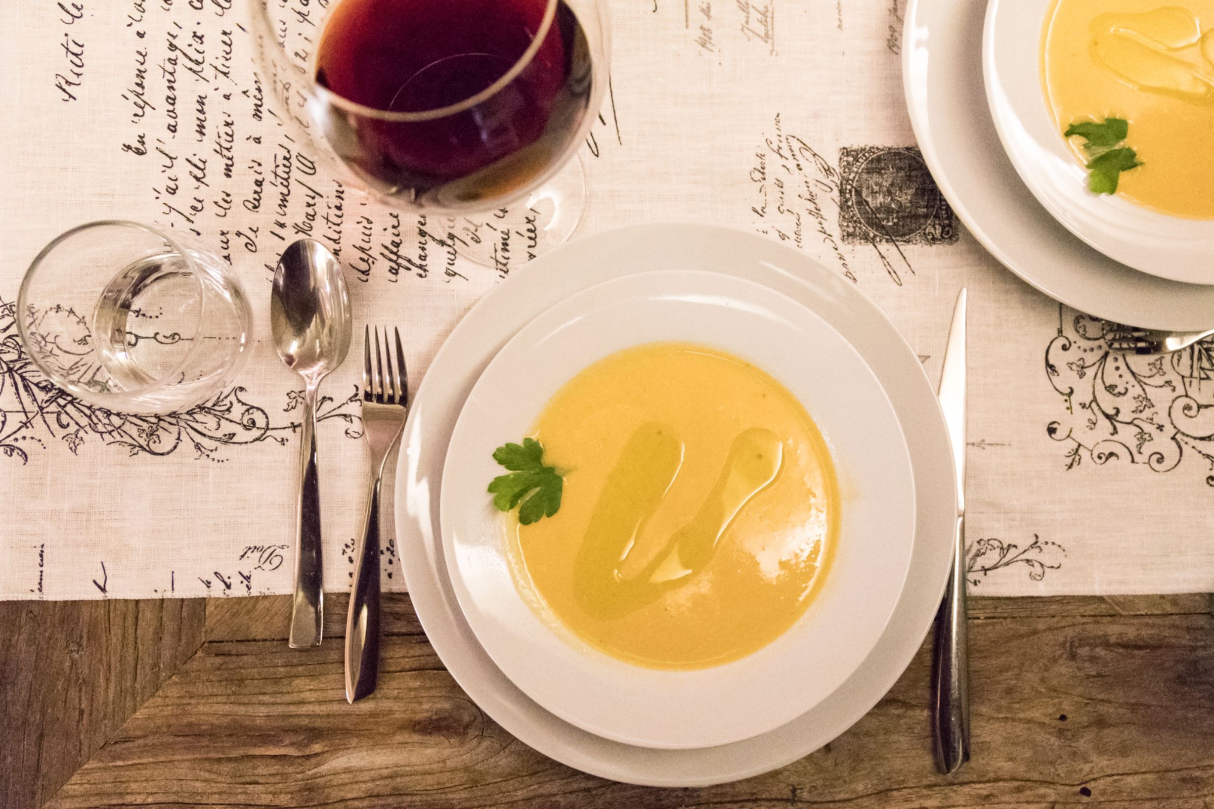 A table setting with a bowl of soup, a glass of red wine, and cutlery.