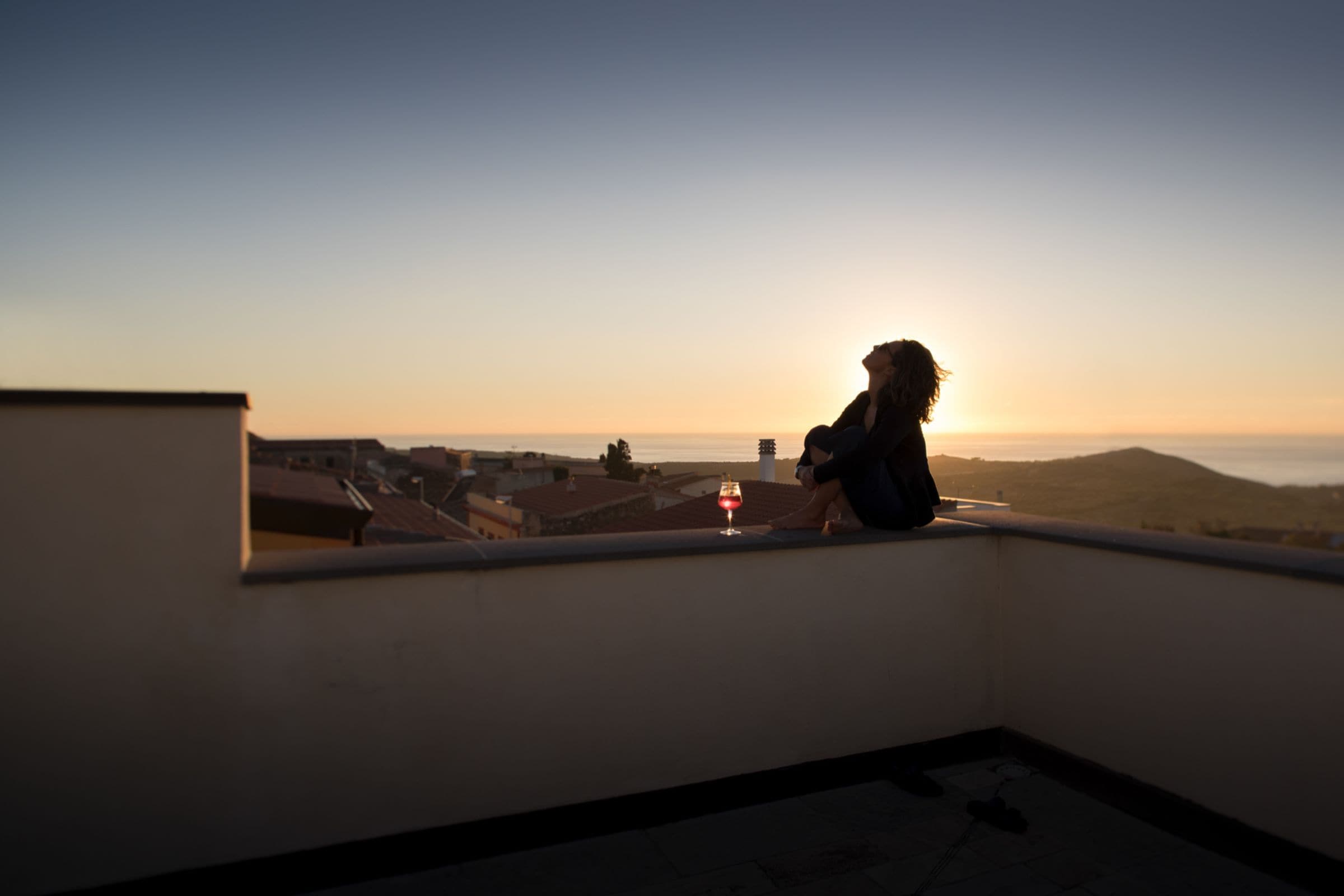 Una persona sentada en un balcón con vistas a un paisaje urbano al atardecer.