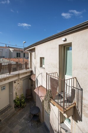 A building with a stone staircase leading to a balcony, a small table, and a potted plant. - Il Cortiletto (Tresnuraghes)