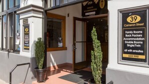 L’entrée d’un hôtel, avec un panneau indiquant la présence de chambres familiales, de chambres pour les routards, d’hébergements, de chambres doubles, de chambres individuelles ou à deux lits, et de salles de bains privatives.