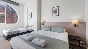 Une chambre d’hôtel avec deux lits, une grande fenêtre, un tableau encadré représentant l’Australie et une table de chevet avec une lampe.