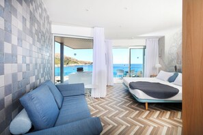 A modern hotel room with a checkered floor, a bed with a blue headboard, a sofa, and a view of the sea. - Mar Azul Hotel - Adults Only (Capdepera)