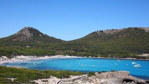 Un paysage côtier avec une plage, des eaux d’un bleu limpide et des collines rocheuses.