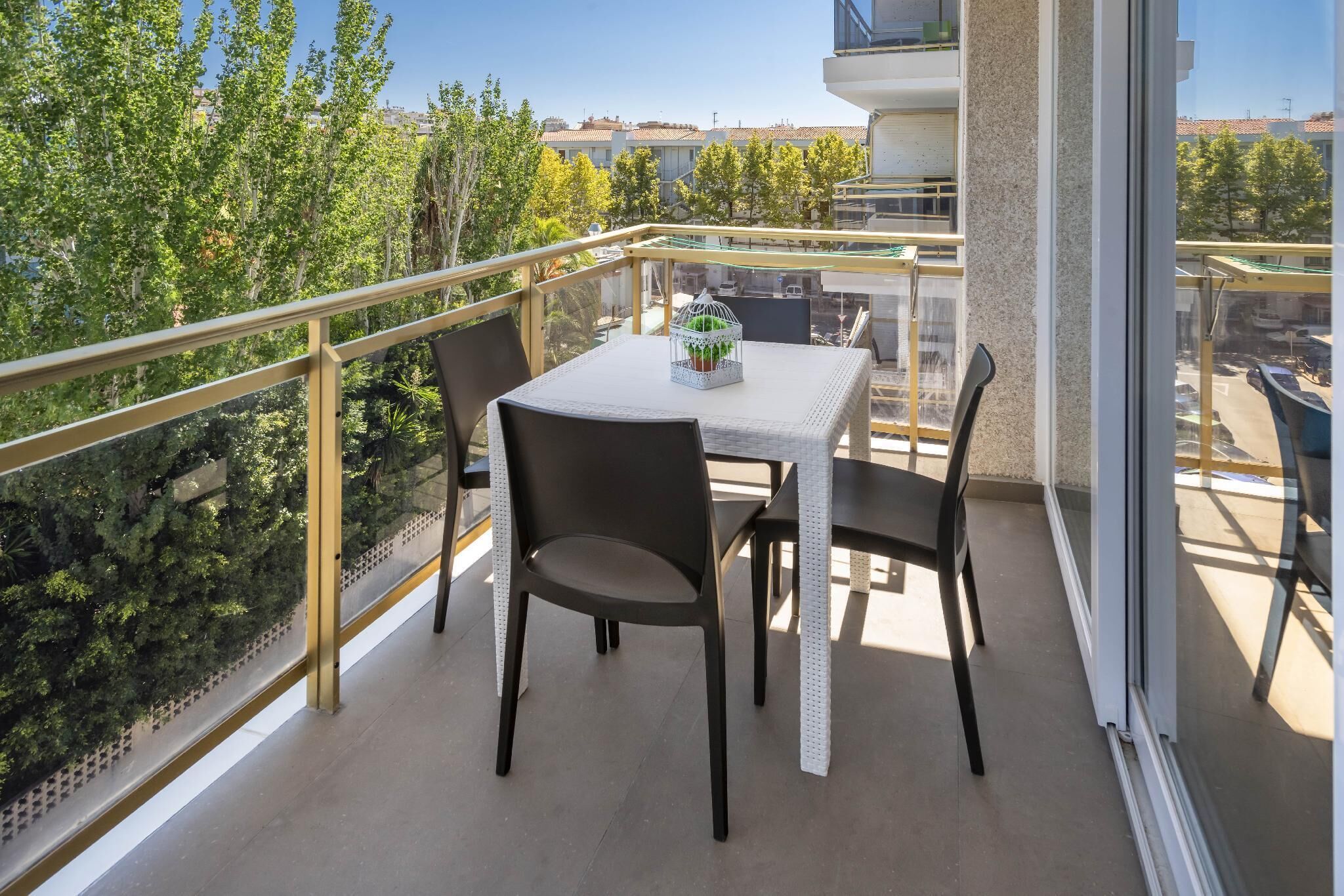 Uma varanda com mesa e cadeiras, uma gaiola de pássaros e vista para árvores e edifícios.