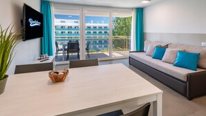 A modern hotel room with a sofa, TV, dining table, and a balcony with a view of buildings. - Rentalmar Playa Salou (Salou)