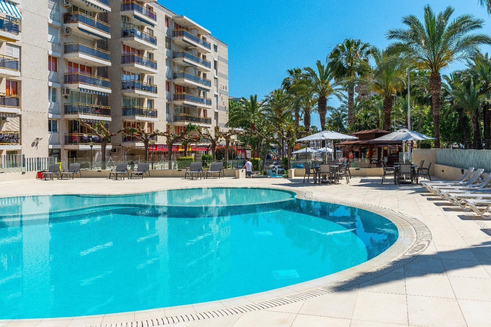 A hotel with a swimming pool, outdoor seating, and palm trees.
