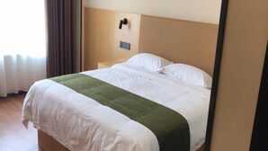 Un letto rifatto con lenzuola bianche e verde, una testiera in legno e un comodino con una lampada.