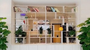 Una libreria bianca con diversi ripiani, alcuni con libri e altri con oggetti decorativi e piante.