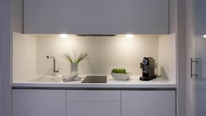 Een moderne keuken met een wit aanrecht, een ingebouwd spoelbakje, een koffieapparaat, een schaal groene appels, een potplant en een witte telefoon.