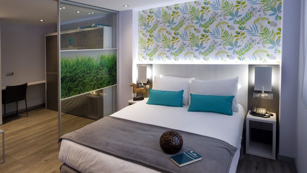 Een moderne hotelkamer met een groot bed, een bureau en uitzicht op groen via een glazen deur.