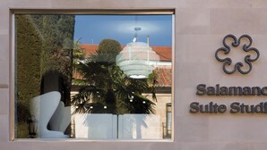 Een hotelschilt voor Salamanca Suite Studios, met een groot raam dat een palmboom en een gebouw met een koepel weerspiegelt.